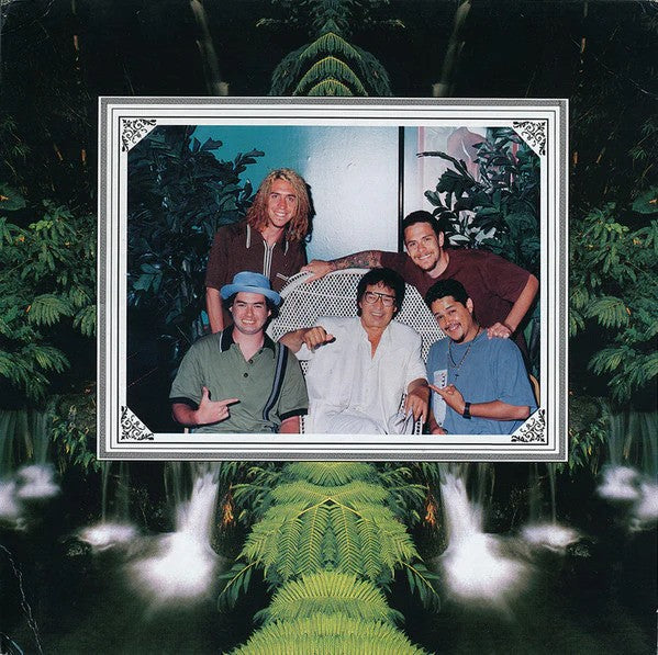 A group of five people pose together, smiling, surrounded by lush green plants and waterfalls. Nearby, a NOFX Black Vinyl LP adds a nostalgic touch to the scene.