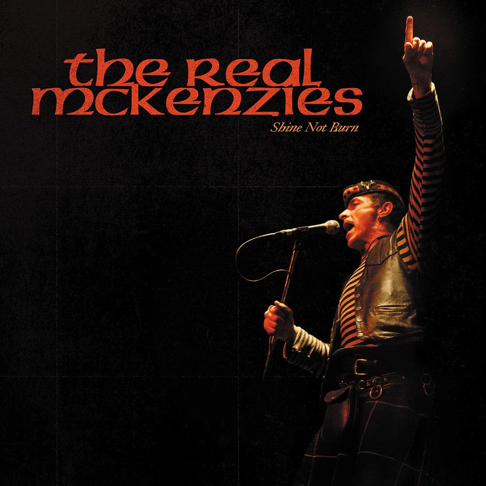 Album cover for the Shine Not Burn CD by Real Mckenzies, showing a performer in striped clothes passionately singing with one arm raised against a dark background and orange text, reflecting Scottish folk music energy.