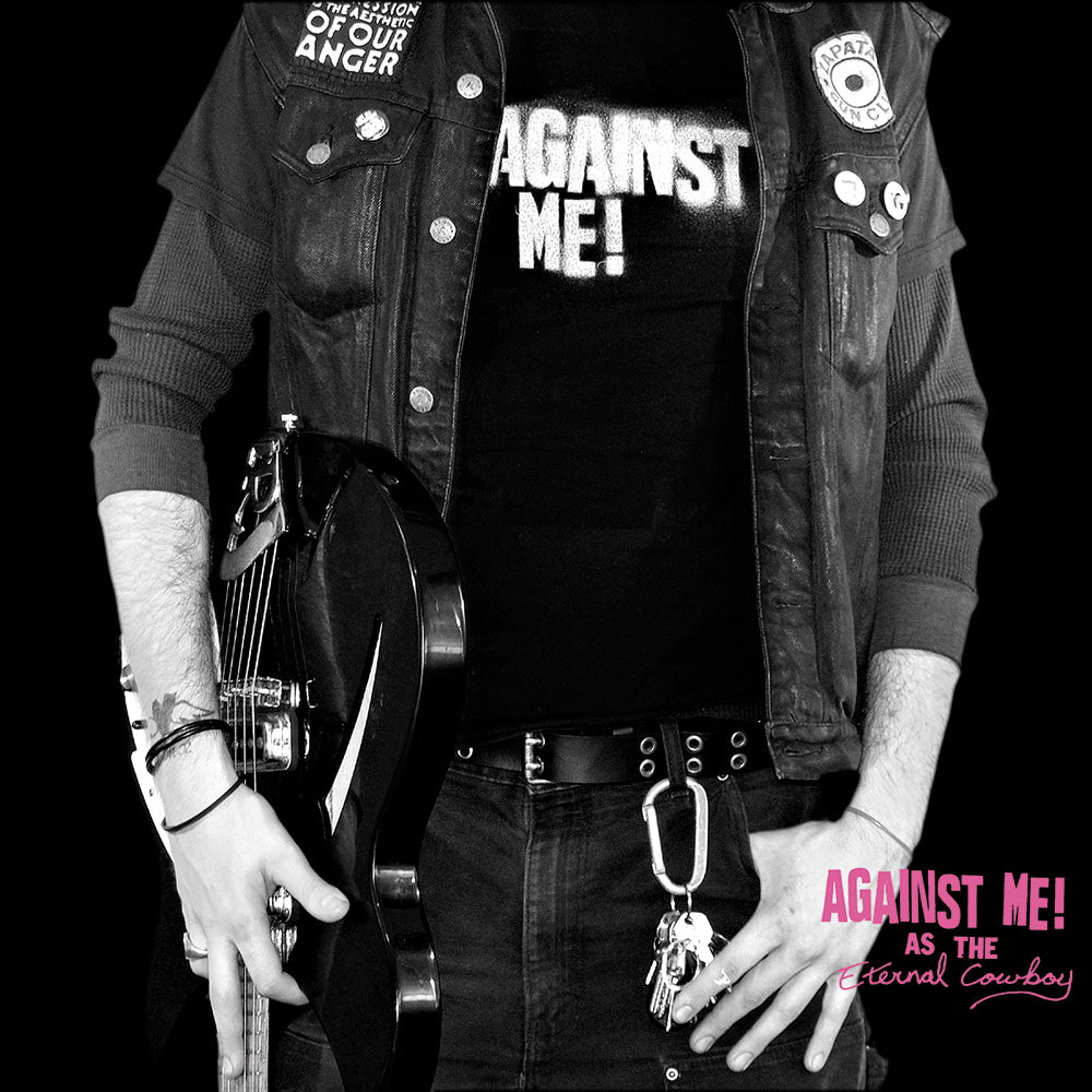 Wearing black clothing and a vest, a person holds an electric guitar. Their shirt says “AGAINST ME!”, the Brand Name. Pink text in the corner reads “AGAINST ME! AS THE Eternal Cowboy.” The background is black.